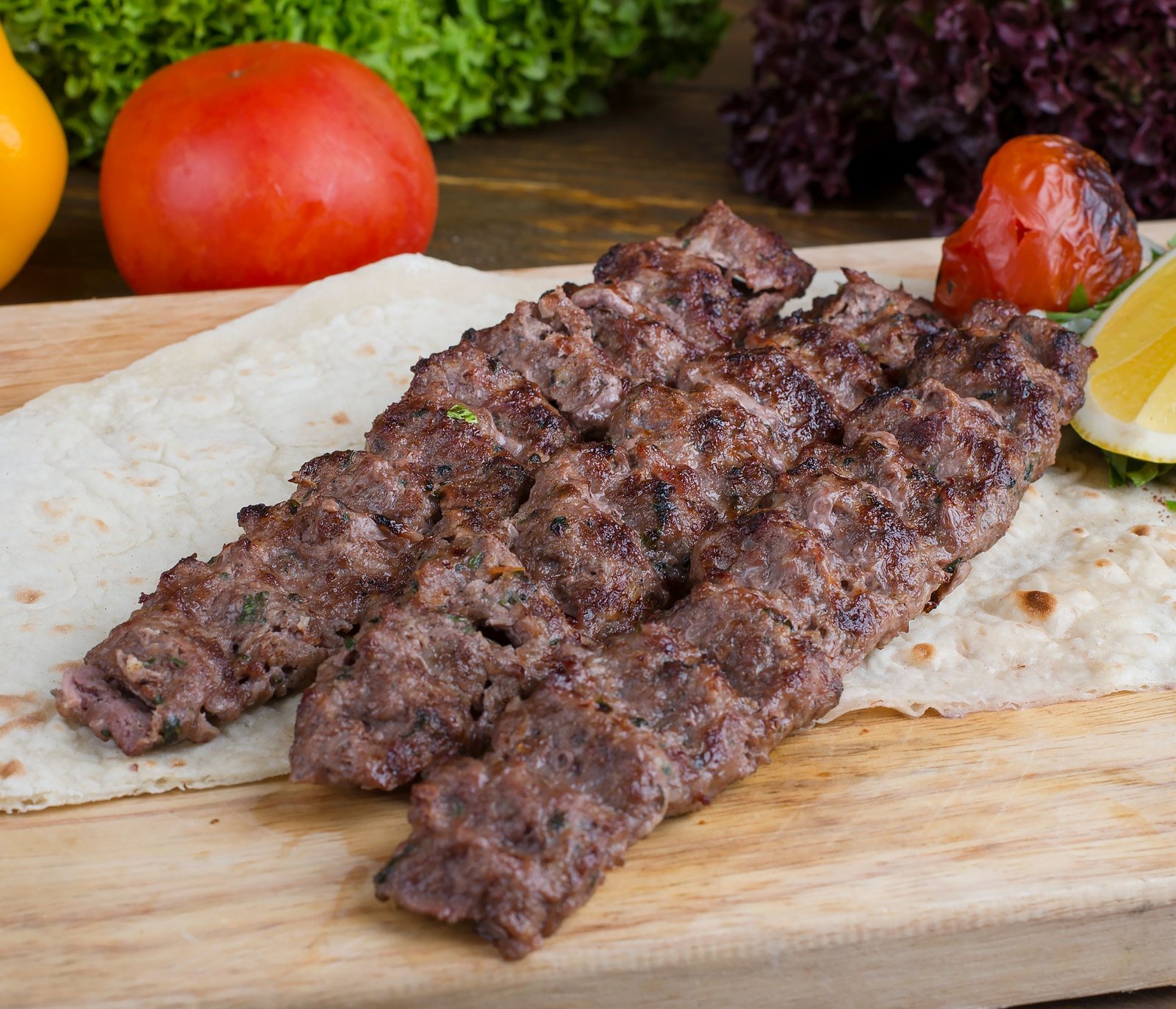 Delicious beef kebab served with fresh vegetables and bread on a wooden platter.