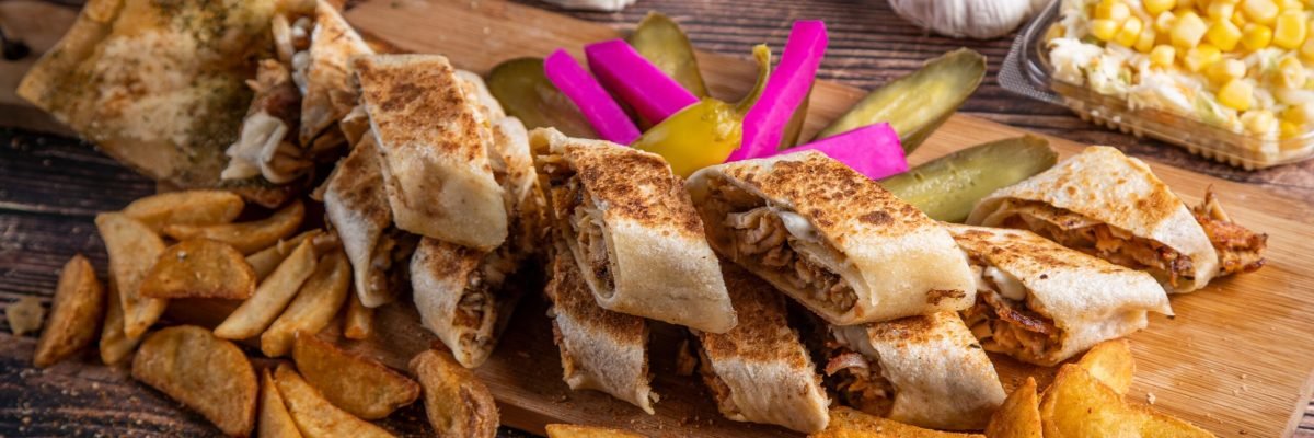 Savory shawarma wrap served with crispy fries, pickles, and sauces on a rustic wooden board.